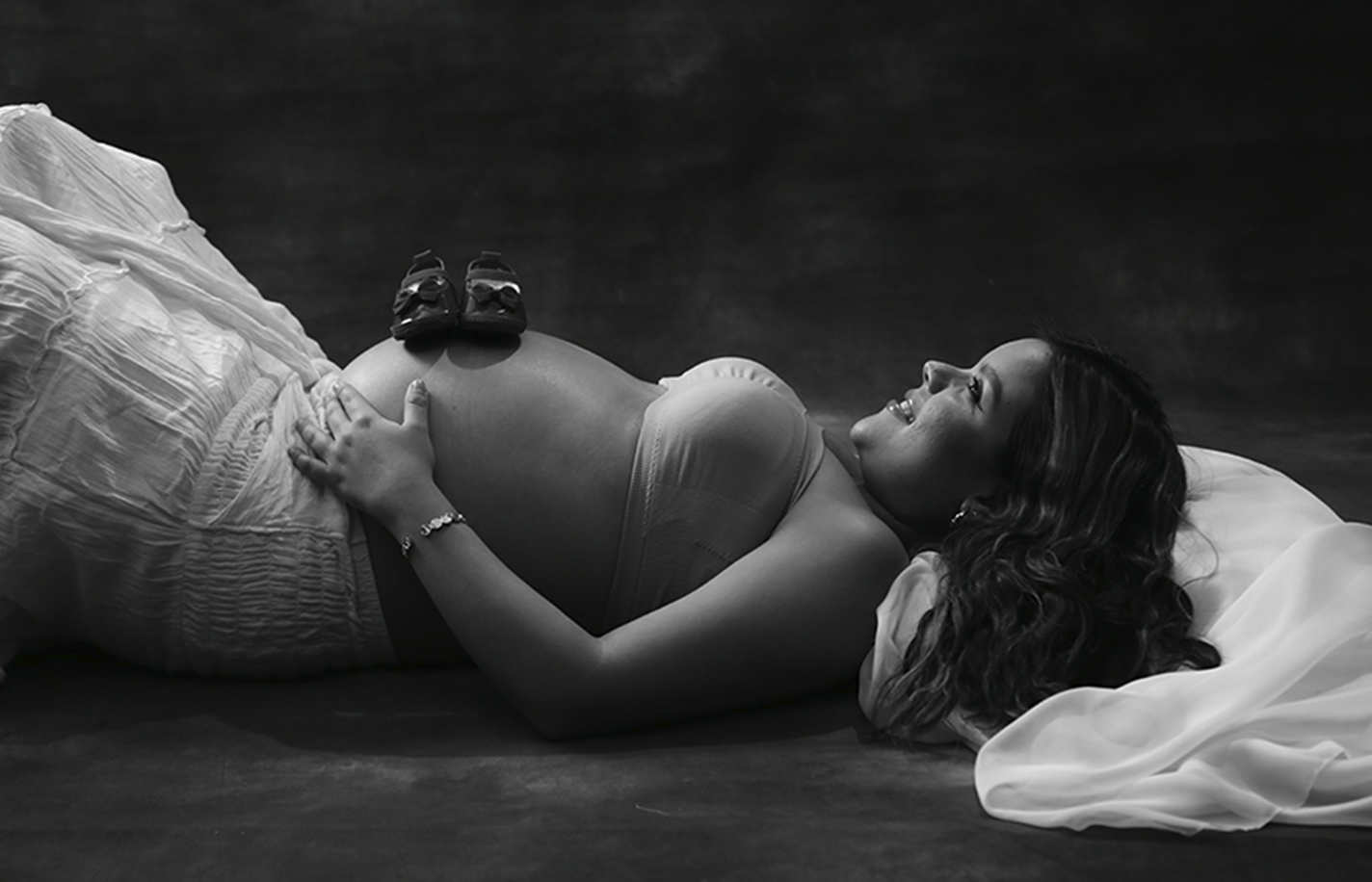 Pregnant woman laying down with baby shoes